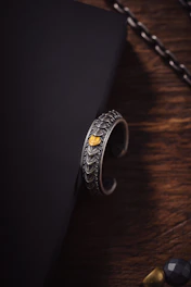 Close-up shot of a minimalist silver cuff bracelet resting on a textured black leather background.