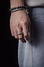 Hands wearing layered rings and bracelets against a concrete urban backdrop.