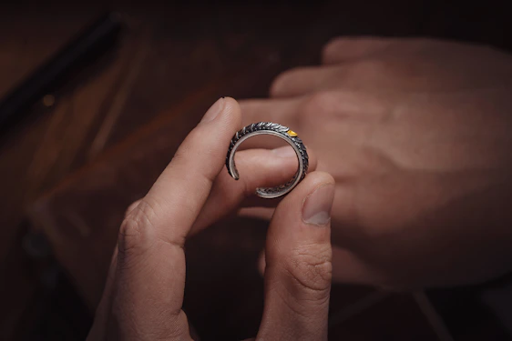 Close-up of a hand delicately holding a polished sterling silver ring against a dark, textured background.