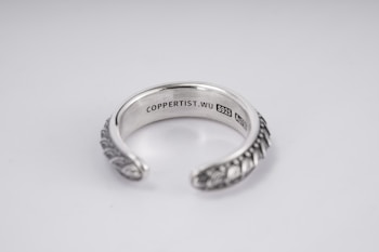 A silver open-ended ring with intricate patterns on the outer surface. The inside is engraved with the text 'COPPERTIST.WU S925 ANT' indicating sterling silver. The design is elegant and detailed, complemented by a smooth inner finish.