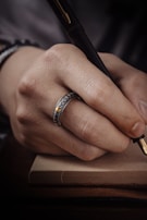 A hand holding a gold pen poised above the elegant cream pages filled with handwritten affirmations.