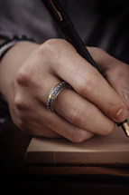 A soft-focus close-up of manicured hands holding a rose gold pen over a booking form on blush pink paper.