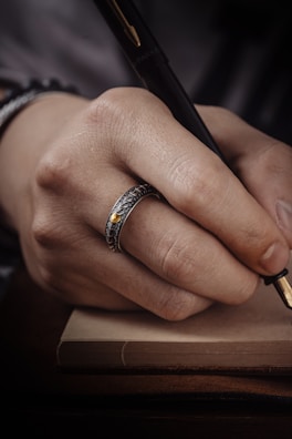 A hand reaching for a sleek fountain pen resting on a leather-bound journal.