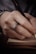 A hand with a decorative ring is holding a black fountain pen, poised over a small hardcover book, suggesting the act of writing or taking notes.