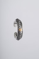 An intricately designed silver ring featuring a textured scale-like pattern and a central gold accent. The ring appears suspended against a plain, light grey background, highlighting its ornate craftsmanship and metallic sheen.