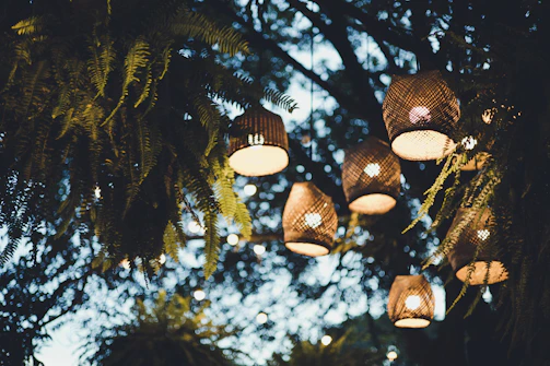 A twilight-lit workshop nestled among ancient trees, with glowing lanterns hanging from branches.