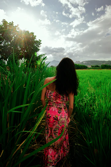 A sunlit scene featuring a woman in a flowing floral summer dress walking through a blooming garden.