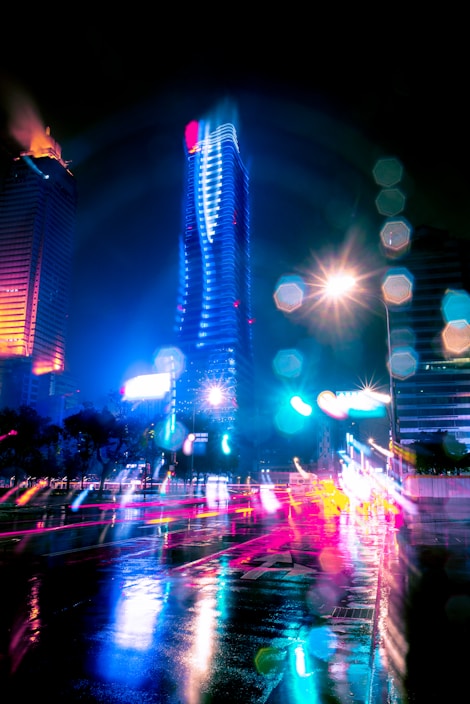 Close-up of a vibrant cityscape at night with colorful lights reflecting on wet streets.