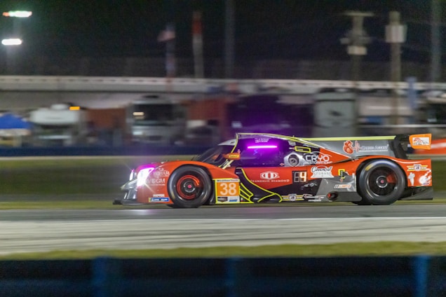 A sleek race car adorned with vibrant sponsor logos speeding on a track under dramatic lighting.