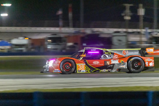 A dynamic racing car speeding on an endurance circuit under bright lights.
