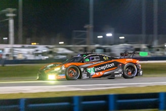 A sleek racing car speeding on a dark track illuminated by orange accent lights.