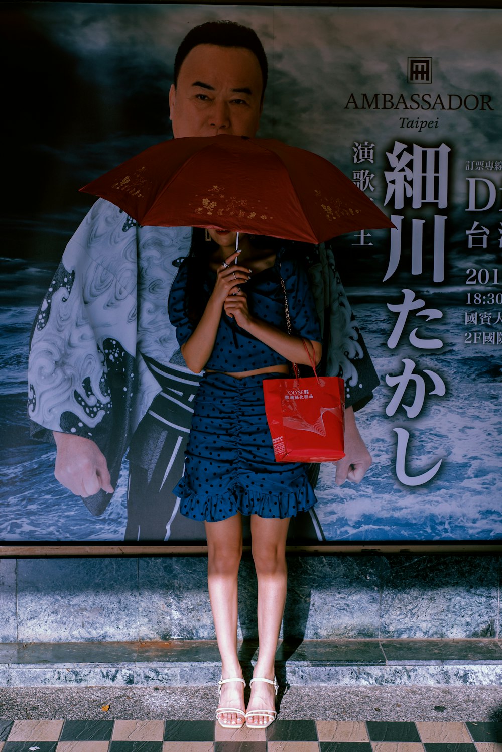 a woman standing under an umbrella in front of a poster