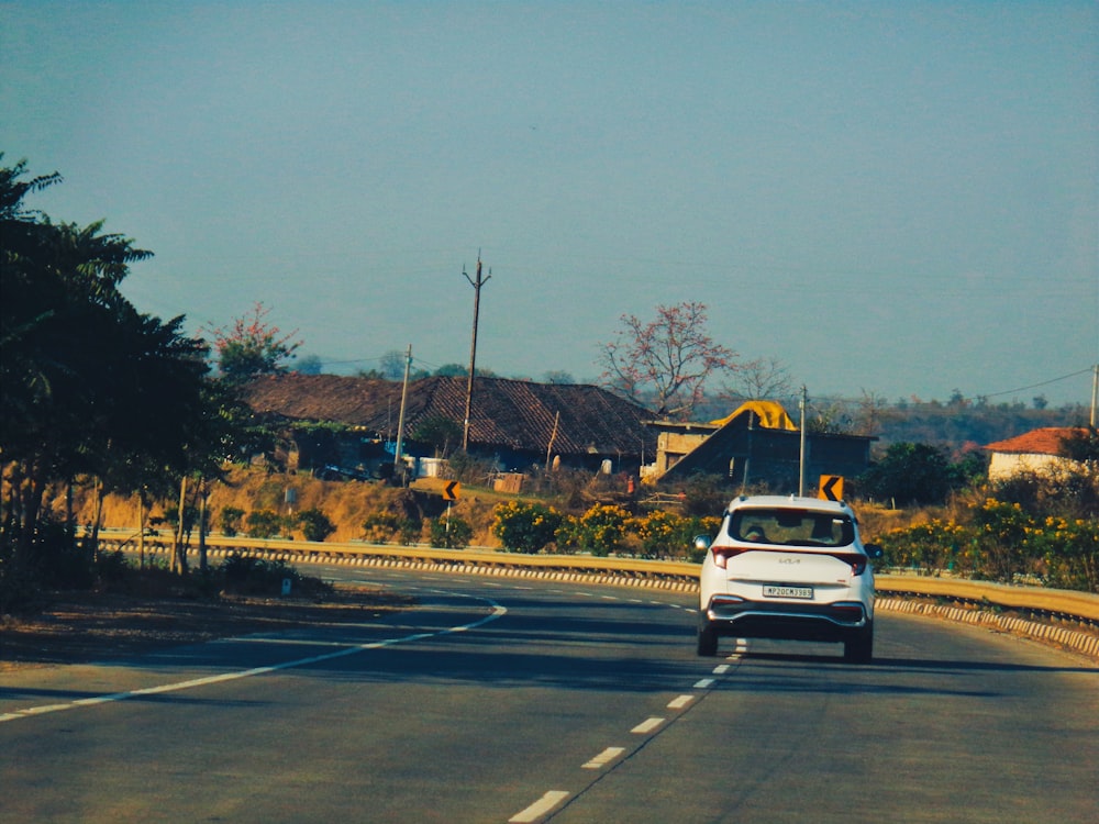 a white car driving down a road next to a forest