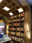 A well-organized bookshelf filled with a variety of books. The shelves are made of light-colored wood with a curved arch design that adds an elegant touch. Books are arranged in an orderly manner, with some positioned vertically while others are stacked horizontally. Light fixtures are integrated into the design, providing a warm and inviting illumination.
