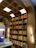 A well-organized bookshelf filled with a variety of books. The shelves are made of light-colored wood with a curved arch design that adds an elegant touch. Books are arranged in an orderly manner, with some positioned vertically while others are stacked horizontally. Light fixtures are integrated into the design, providing a warm and inviting illumination.