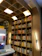A well-organized bookshelf filled with a variety of books. The shelves are made of light-colored wood with a curved arch design that adds an elegant touch. Books are arranged in an orderly manner, with some positioned vertically while others are stacked horizontally. Light fixtures are integrated into the design, providing a warm and inviting illumination.