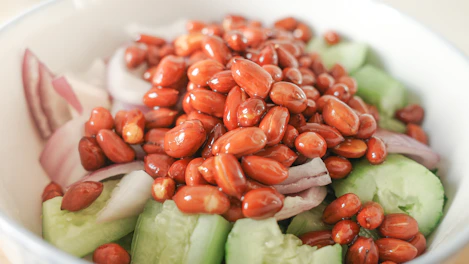 A colorful bowl of fresh salad drizzled with a golden peanut dressing, set on a deep brown wooden table.