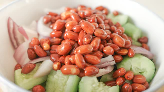 A colorful bowl of fresh salad drizzled with a golden peanut dressing, set on a deep brown wooden table.