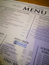 A menu from a restaurant titled 'Old Prague Menu' featuring sections for main courses, international dishes, beer, wine, and alcoholic beverages. The menu lists various Czech dishes with prices in Czech koruna. It includes items like grilled steak, dumplings, chicken wings, and different types of Staropramen beer.