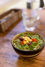 Bright and colorful bowl of fresh salad with a variety of greens, tomatoes, and seeds on a wooden table.