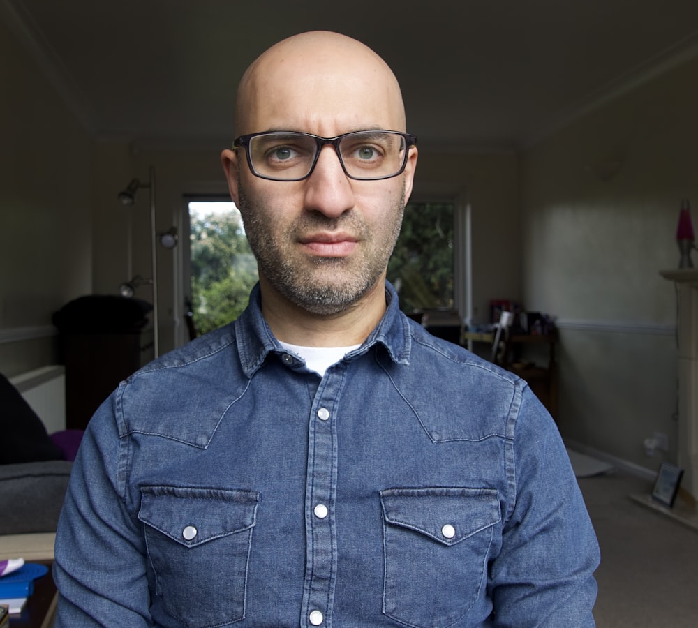 a bald man wearing glasses and a denim shirt