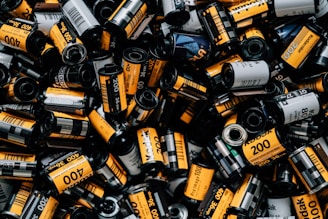 A collection of numerous Kodak film rolls displaying a variety of labels, predominantly with bold yellow and black colors. The rolls are scattered and densely packed, showcasing various film types such as 200 and 400 ISO.