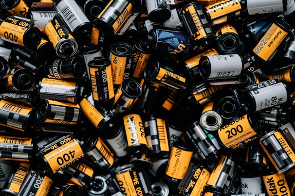 A collection of numerous Kodak film rolls displaying a variety of labels, predominantly with bold yellow and black colors. The rolls are scattered and densely packed, showcasing various film types such as 200 and 400 ISO.