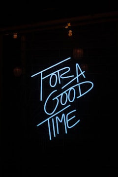 Neon blue letters spell out 'FOR A GOOD TIME' against a dark background, creating a striking visual contrast. The surrounding area is dimly lit, enhancing the brightness and vibrancy of the neon text.