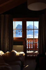 Interior view of a cabin showing a warm, inviting bed with natural light streaming through large windows.