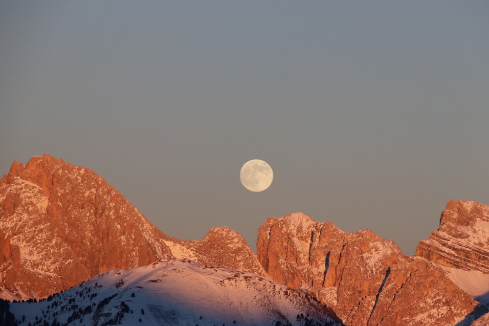 a full moon rising over a mountain range