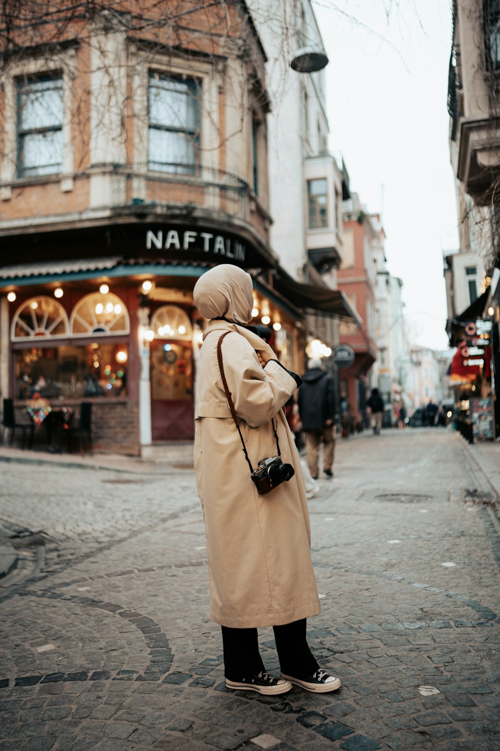 a woman in a trench coat standing on a street corner