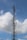 A tall metal telecommunications tower extends into the sky, surrounded by white clouds. The structure includes several antennas and dishes, indicating its use for broadcasting or communication.