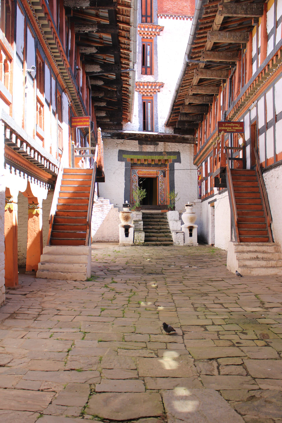 The sunlit flagstone courtyard of a dzong in Trongsa district, wooden stairs to painted galleries