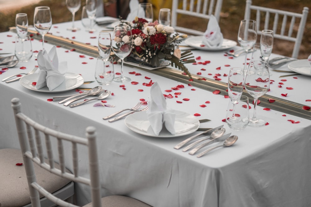a table set for a formal dinner with red rose petals on the table