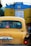 A yellow taxi is seen in traffic with a blue and yellow vehicle in front of it. The taxi has a registration plate and religious stickers on the rear window. There is text in a regional script on the back of the taxi.