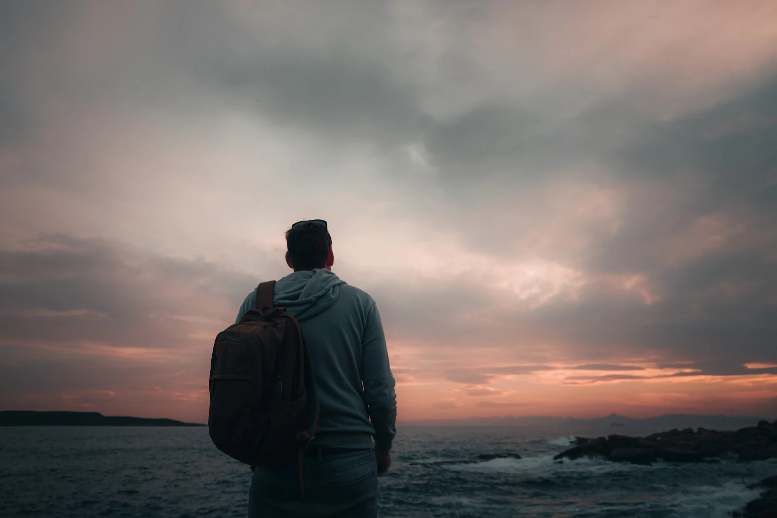 Man with a backpack looking out at the ocean, taking time for self-reflection and growth after a breakup