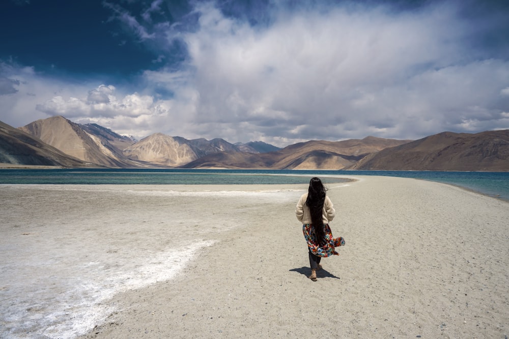 a woman standing on a beach with mountains in the background