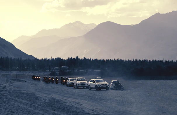 A panoramic view of the convoy of motorcycles and 4x4s winding through a narrow mountain road.