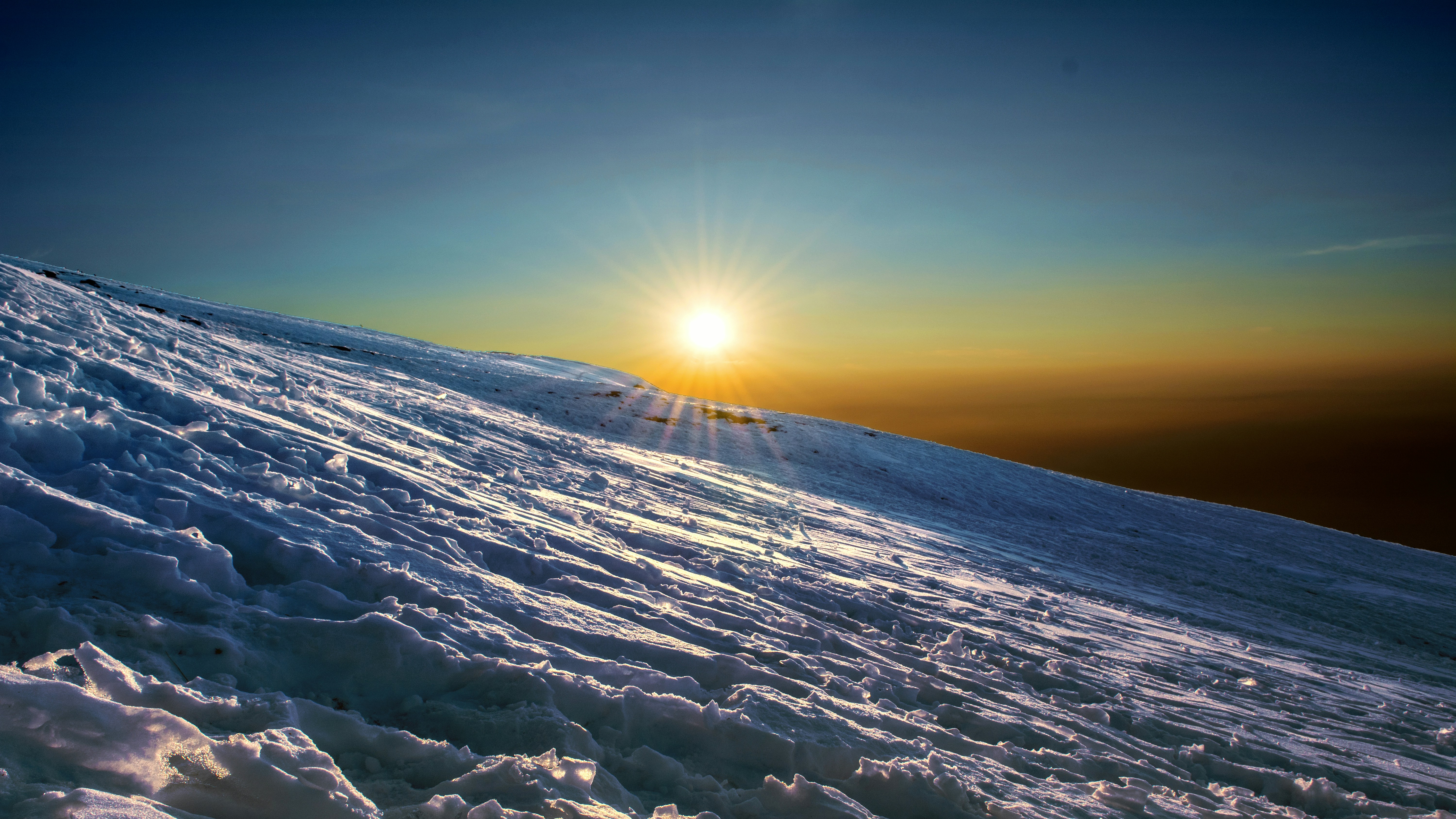the sun is setting over a snowy mountain