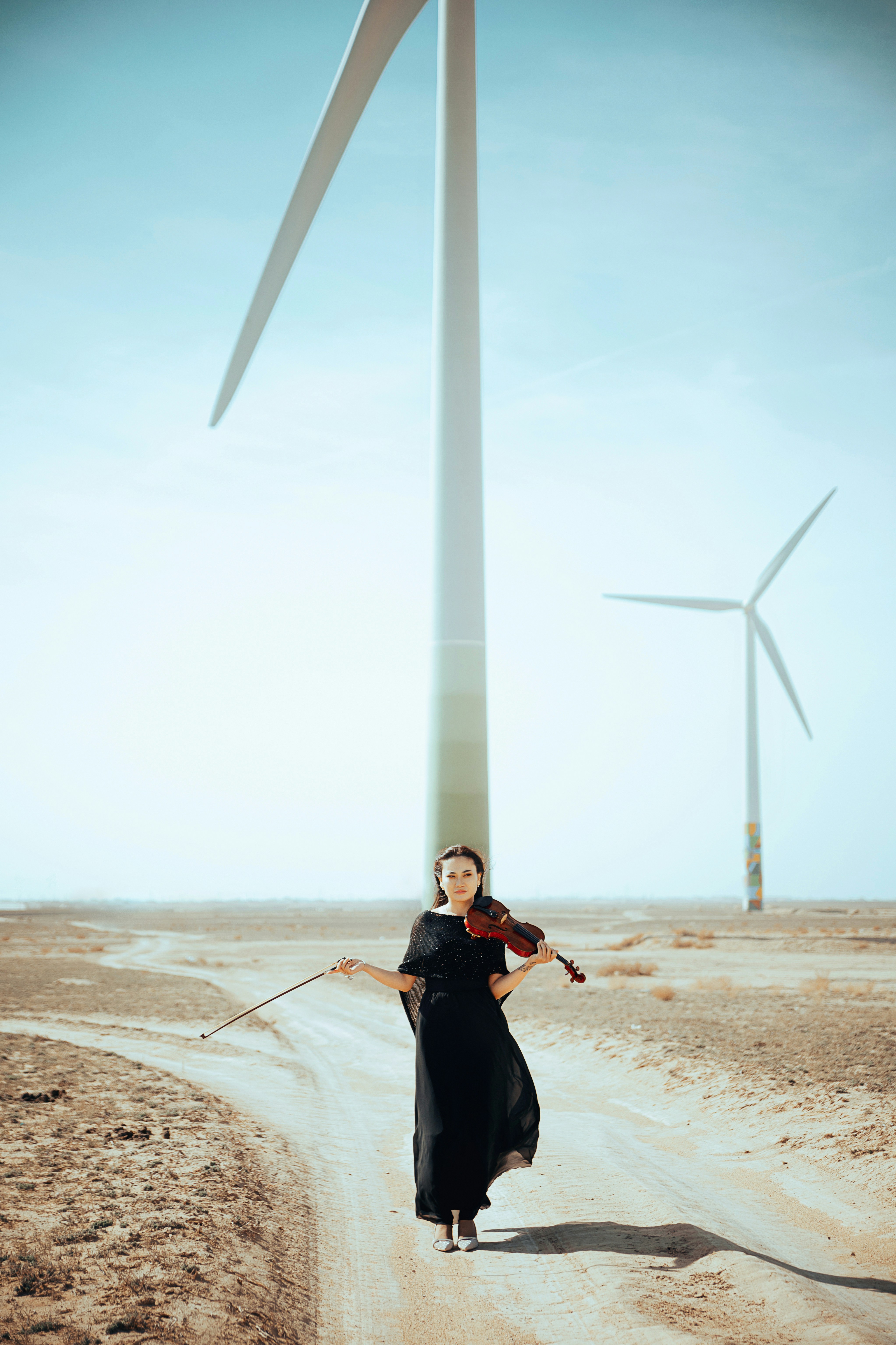 Una mujer con un vestido negro tocando el violín frente a una turbina eólica