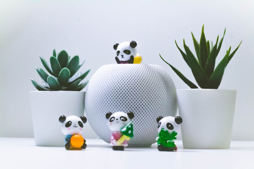 a group of toy panda bears sitting next to a potted plant