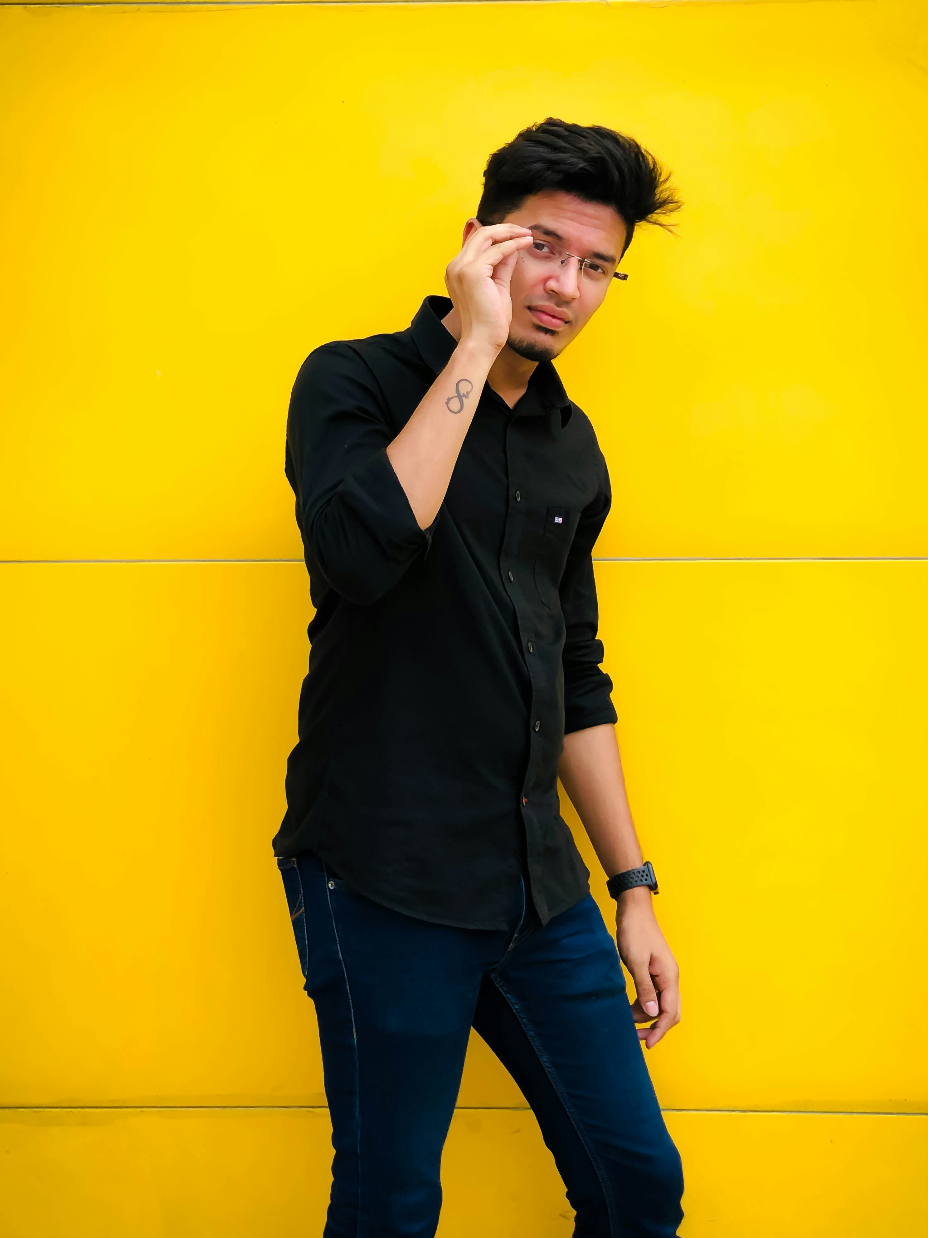 a man standing against a yellow wall talking on a cell phone