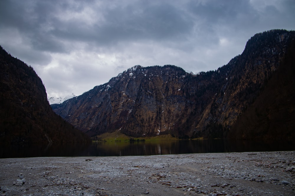 a lake surrounded by mountains under a cloudy sky