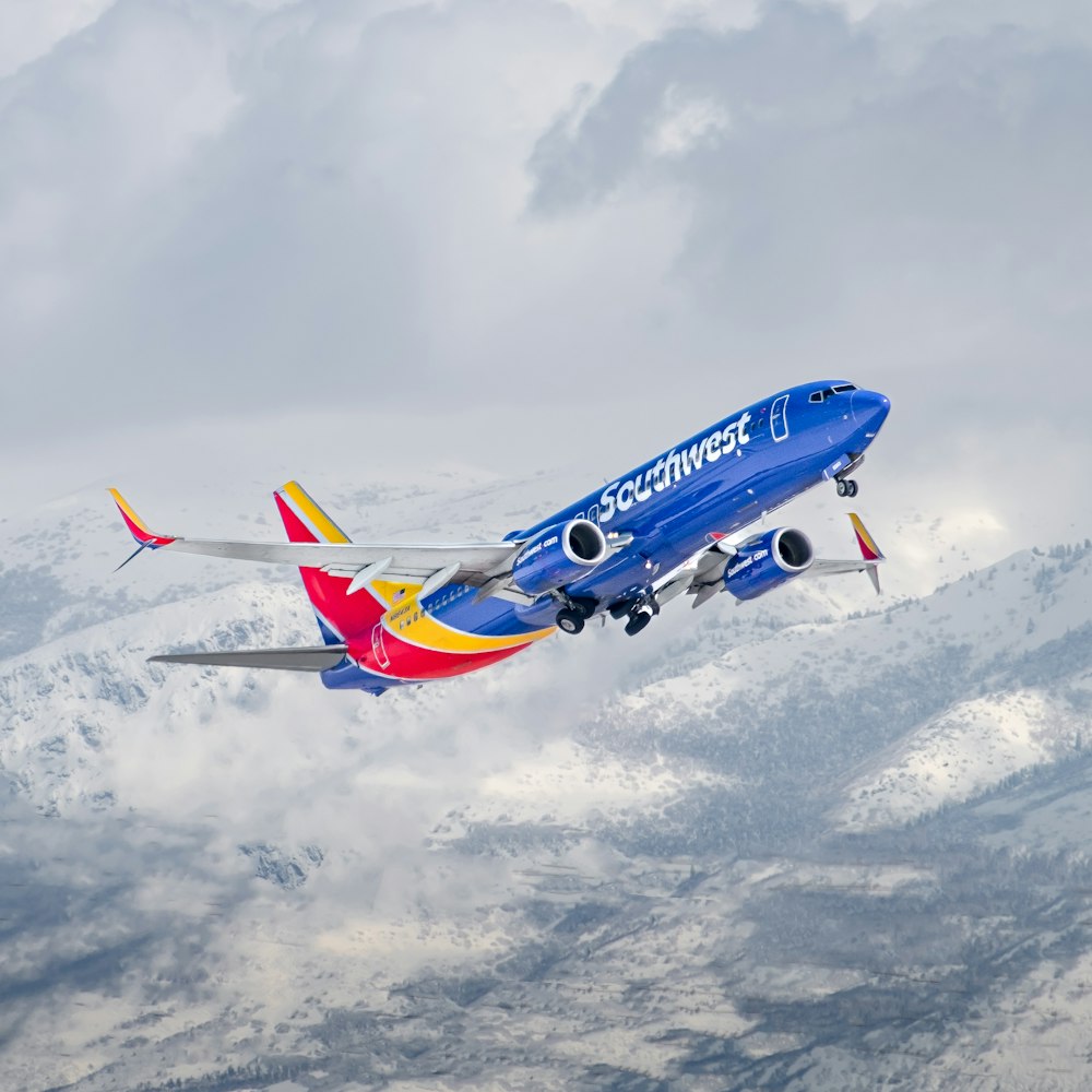 a blue and yellow plane flying over a mountain