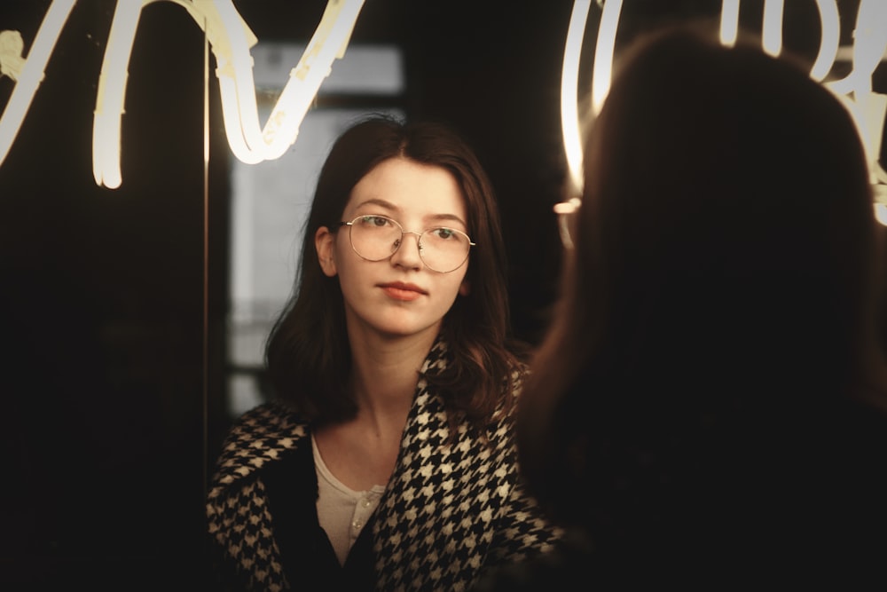 a woman with glasses looking in a mirror