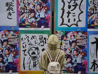 A person wearing a light green jacket and carrying a white backpack is standing in front of a wall adorned with vibrant and colorful posters. The posters feature dynamic images of people in various engaging activities, with one showing people in school uniforms holding musical instruments and another featuring bold Japanese text with graphic designs.