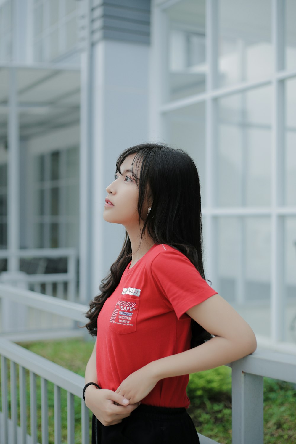 a woman in a red shirt leaning against a fence