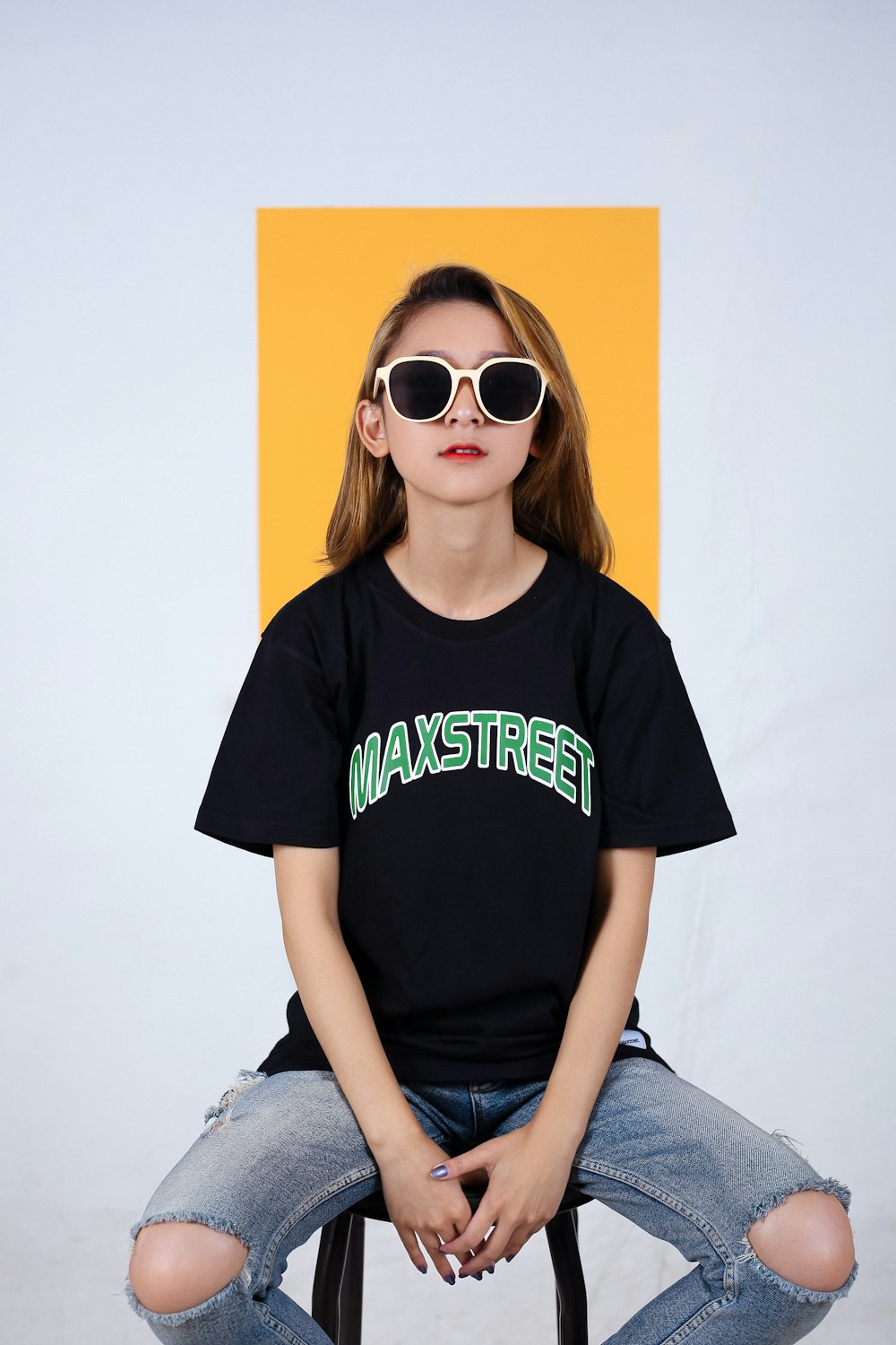 a girl sitting on a stool wearing sunglasses