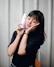 Smiling woman with glowing skin holding a skincare product from Brilhoviva in a bright, modern room.