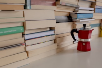 a stack of books next to a red coffee pot